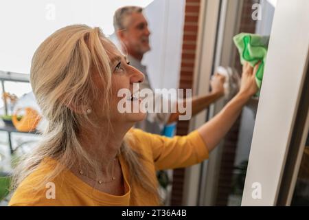 Donna felice che pulisce la finestra della casa Foto Stock