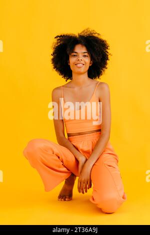 Donna sorridente inginocchiata su sfondo giallo Foto Stock