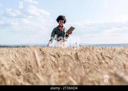 Sorridente lavoratore afro che tiene un tablet PC sul campo per esaminare il raccolto di orzo Foto Stock