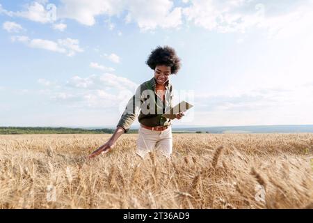 Giovane agronomo afro sorridente con un tablet PC che esamina l'orzo sul campo Foto Stock