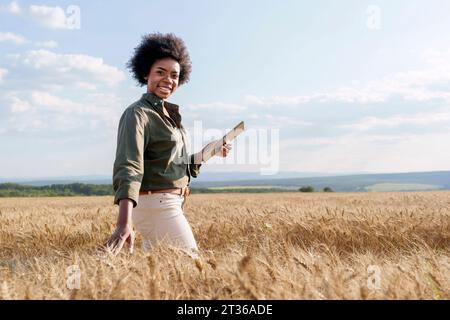 Sorridente giovane agricoltore afro con un tablet PC in un campo di orzo Foto Stock