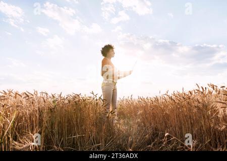 Giovane lavoratore agricolo che tiene un computer portatile in un campo d'orzo Foto Stock