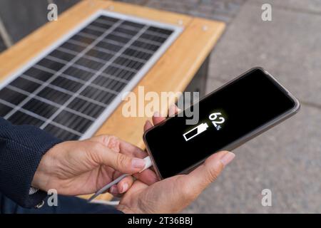 Mani di donna d'affari che caricano lo smartphone utilizzando l'energia solare sul banco Foto Stock
