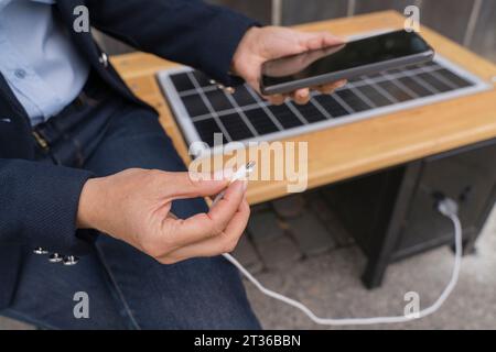 Donna d'affari che collega il cavo USB allo smartphone al punto di ricarica solare Foto Stock