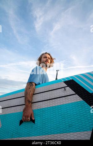 Giovane che porta il paddleboard sotto il cielo Foto Stock