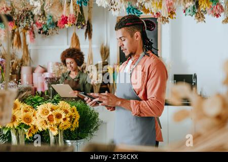 Fiorista che utilizza un tablet PC in piedi vicino a un collega tra i fiori del negozio Foto Stock