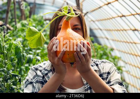 Giovane agricoltore che tiene squash appena raccolto in serra Foto Stock