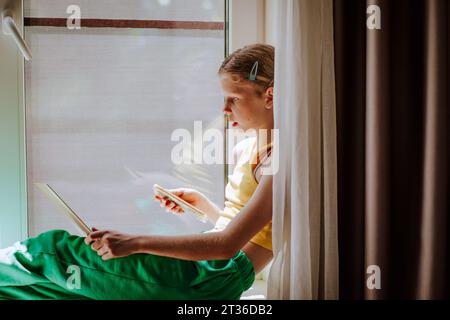 Ragazza con smartphone che usa un notebook a casa Foto Stock