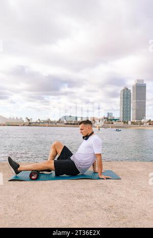 Addestramento giovanotto con fascia rotolare su molo di cemento vicino al mare Foto Stock