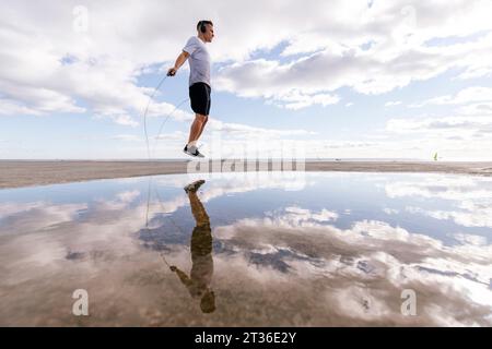 Giovane che salta la corda vicino alla pozzanghera sul molo Foto Stock