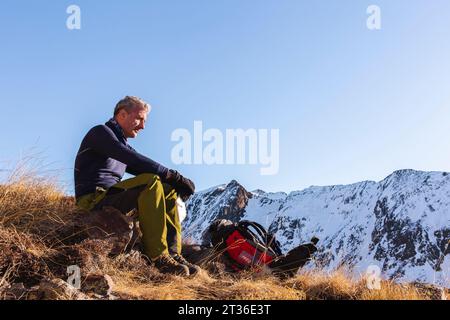 Uomo contemplativo seduto con zaino in montagna in inverno Foto Stock