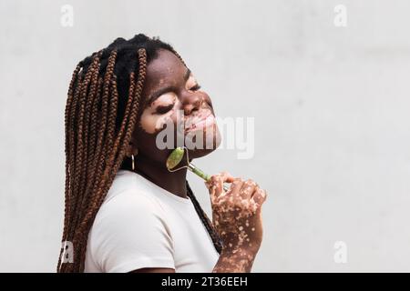Giovane donna sorridente con rullo di giada davanti al muro bianco Foto Stock