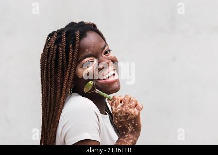 Giovane donna felice con il rullo di giada davanti al muro bianco Foto Stock