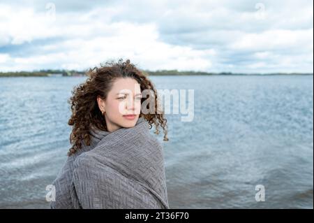 Donna contemplativa con capelli ricci avvolti in scialle in acqua Foto Stock