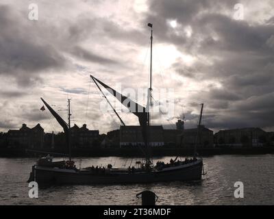 Limehouse, Londra, Regno Unito - 21 ottobre 2023: La chiatta a vela del Tamigi sarà in silhouette, passando tra Limehouse e Rotherhithe. Foto Stock