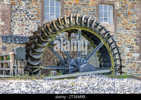 Vecchio mulino ad acqua EPER o Wingbergermolen sul fiume Geul, parete in pietra con due finestre, con supporto, ruota rotante, albero e lame, giornata di sole a te Foto Stock