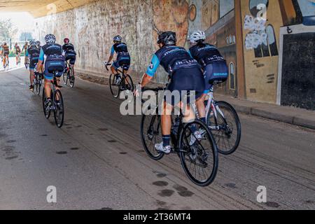 Beek, Limburgo meridionale, Paesi Bassi. 17 settembre 2023. Vista posteriore di un gruppo di ciclisti su strada rurale, sotto un ponte con luce solare alla fine del tunnel in b Foto Stock