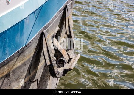 Primo piano dell'ancora di ormeggio sul lato della nave da carico, sporco e arrugginito, combinazione di colori bianco, blu e nero, riflesso della luce solare sulla superficie dell'acqua Foto Stock
