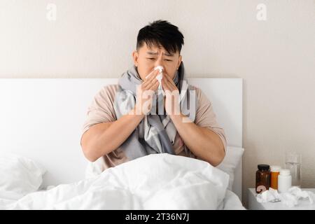 Uomo asiatico di mezza età malato che indossa pigiama e sciarpa calda Foto Stock