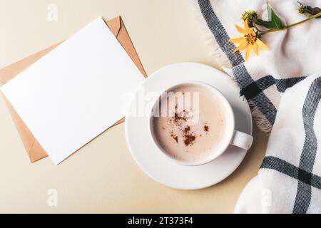 Una tazza di cappuccino piccante e carta bianca, quadri e fiori gialli su sfondo verde oliva. Vista dall'alto, base piatta, mockup. Foto Stock