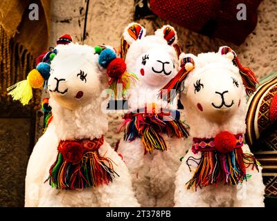Giocattoli sorridenti di peluche di alpaca decorati con archi color arcobaleno, mercato tradizionale di Pisac, Perù Foto Stock