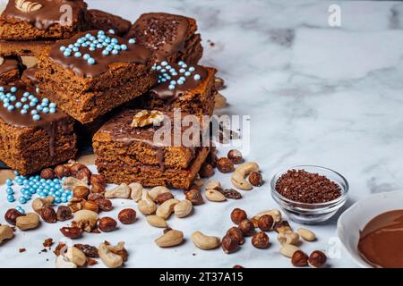 Brownie ripieni di marmellata e ingredienti per la decorazione, glassa di cioccolato, miscela di noci, cospargi di cioccolato, perle di zucchero, copia spazio Foto Stock