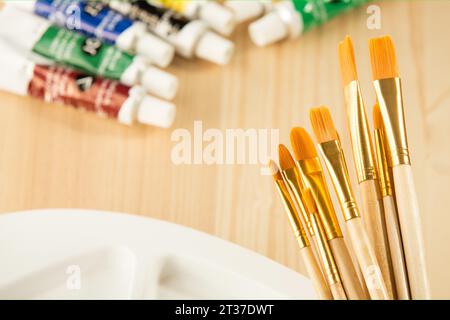 Nuovo set di pennelli puliti di diverse dimensioni su un manico in legno, con set di colori acrilici, la tavolozza dell'artista su uno sfondo in legno. Artistico Foto Stock