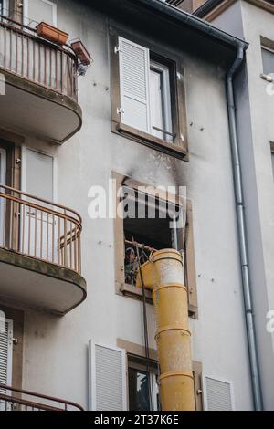 Strasburgo, Francia - 22 novembre 2023: Un lavoratore vicino a secchio giallo vicino a una finestra di un edificio urbano, che pulisce i detriti dopo un incendio all'interno Foto Stock