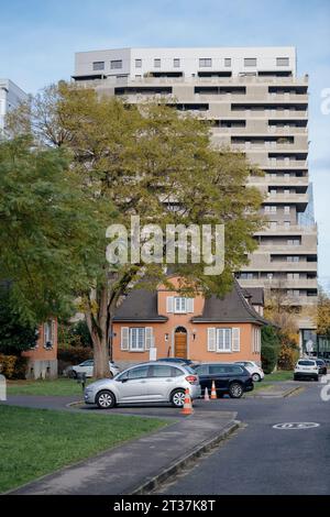 Strasburgo, Francia - 22 novembre 2023: Un edificio alto e moderno che torreggia dietro una tradizionale casa arancione, circondato dal verde e dalle auto parcheggiate in una strada tranquilla Foto Stock