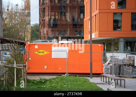 Strasburgo, Francia - 22 novembre 2023: Un contenitore arancione con l'insegna della COLAS Construction Corporation si trova accanto a un alto cantiere edile, racchiuso da una recinzione protettiva. Foto Stock