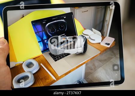 Parigi, Francia - 6 giugno 2023: Un'immagine su un tablet iPad mostra una scrivania in legno con un laptop che mostra futuristici occhiali Vision Pro, un visore VR a righe appoggiato sulla tastiera, accessori per cuscinetti auricolari abbinati, uno stilo e uno smartphone rosa Foto Stock