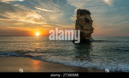 Le sfumature arancioni riempiono il cielo mentre il sole tramonta sulla spiaggia di Dona Ana a Lagos, Algarve, Portogallo Foto Stock