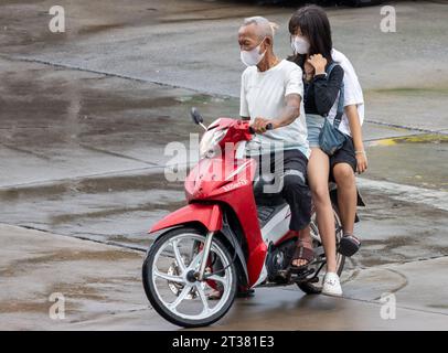 SAMUT PRAKAN, THAILANDIA, 13 ottobre 2023, un vecchio guida una moto con due donne in una strada piovosa Foto Stock