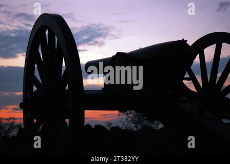 Un cielo al tramonto nel parco militare nazionale di Gettysburg rende un cannone della guerra di secessione americana in silhouette e il campo di battaglia in silenzio Foto Stock