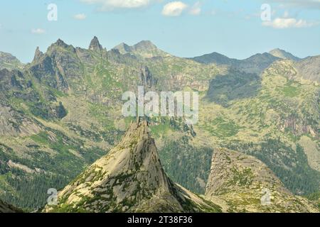 Una grande roccia a due teste con ripidi pendii sullo sfondo di picchi di montagna appuntiti in una soleggiata giornata estiva. Parabola Rock, Parco naturale Ergaki, Foto Stock