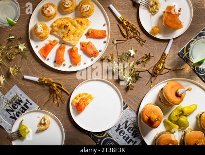 Cenone di Capodanno con decorazioni. salmone, pantofole, peperoni e margarita su un tavolo di legno, vista dall'alto Foto Stock