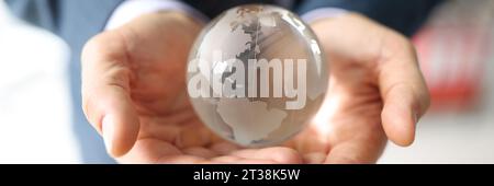 Uomo in tuta da lavoro tiene globo di vetro con continenti Foto Stock