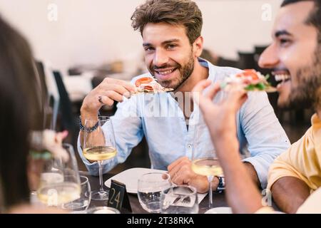 Un gruppo di giovani gusta una pizza gourmet in un ambiente rilassato, con bicchieri da vino che migliorano l'esperienza culinaria - amici che si godono la pizza Foto Stock