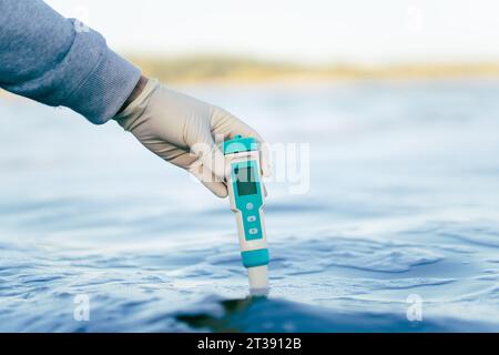 esame della qualità dell'acqua in un serbatoio naturale. un dispositivo per misurare le impurità nell'acqua nella mano maschile di uno specialista scientifico. Foto Stock