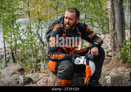 REPUBBLICA DI CARELIA, RUSSIA - GIUGNO 2022 CIRCA: Torneo fuoristrada Ladoga Trophy 2022 in Carelia. Un motociclista sportivo stanco riposa nella natura durante una gara Foto Stock