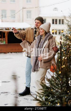 Un uomo che mostra qualcosa alle donne al mercatino di natale in un look invernale Foto Stock