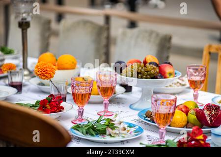 Un vivace tavolo all'aperto con un assortimento di frutta fresca, bicchieri colorati pieni di bevande e fiori decorativi posti su un bianco Foto Stock