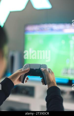 Vista posteriore delle mani di una giocatrice anonima che utilizza il joystick mentre gioca a un videogame in TV nel salotto di casa durante il fine settimana Foto Stock