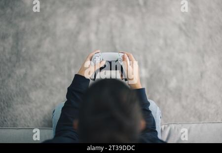 Vista dall'alto delle mani di una giocatrice anonima che utilizza il joystick mentre gioca a un videogame in salotto a casa durante il fine settimana Foto Stock