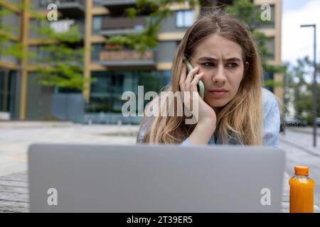 Vista ravvicinata di uno studente dai capelli biondi serio che parla con lo smartphone in città. Foto Stock