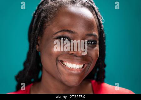 Donna africana con capelli intrecciati e camicetta rossa, catturata dal collo, su uno sfondo turchese Foto Stock