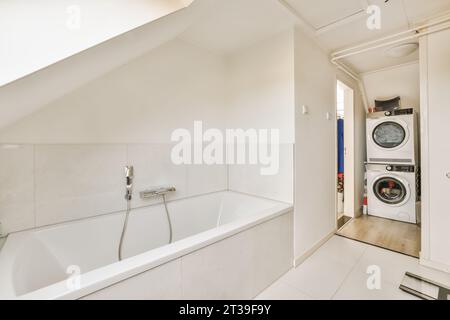 Interno di un piccolo bagno bianco con vasca in ceramica e lavatrici e asciugatrici in un moderno appartamento luminoso Foto Stock