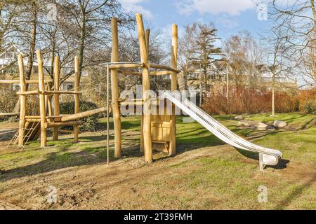 Scivolo vuoto e attrezzatura da gioco in legno contro alberi e piante nel parco giochi durante la giornata di sole Foto Stock
