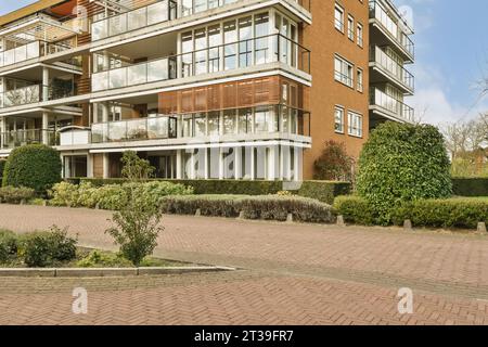 Esterno di un moderno edificio residenziale con cespugli che crescono davanti alla strada pavimentata durante il giorno Foto Stock