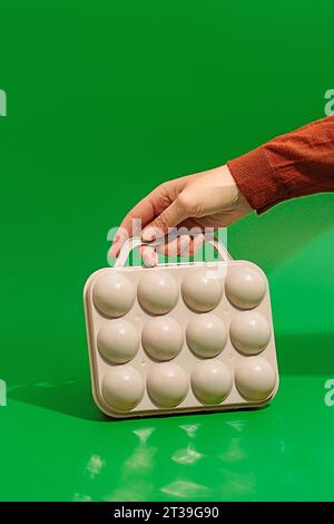 Mano di una persona anonima che tiene in mano una scatola da golf in plastica color crema posizionata su una superficie verde con luce solare brillante sullo sfondo all'esterno Foto Stock